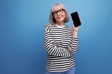 60 'lı yaşlarda orta yaşlı bir kadın elinde akıllı bir telefon ve fotokopi alanı olan parlak bir arkaplan tutuyor..