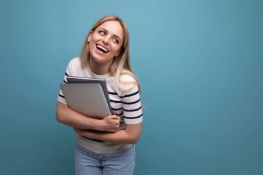 Elinde dizüstü bilgisayarı olan kendine güvenen genç bir kız öğrenci kopya alanı olan mavi izole bir arka planda..