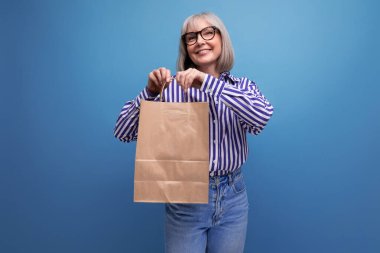 60 'lı yaşlarda, orta yaşlı, beyaz saçlı, şık görünümlü bir kadın. Elinde fotokopi alanı olan parlak bir stüdyo arkaplanı olan el işi bir çanta tutuyor..