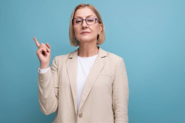 Kendine güveni tam, kısa saçlı, klasik ceketli yetişkin bir kadın fotokopi alanı olan parlak bir arka planda duruyor..