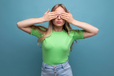 Sarışın genç bir kadın ellerini mavi izole bir arka plana koyup gözlerini kapadı..