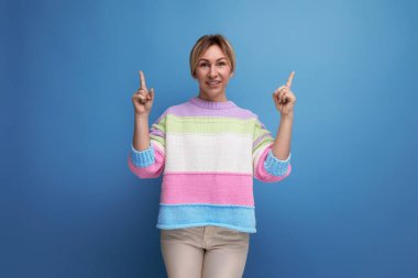 Çizgili süveter giyen hoş, çekici sarışın genç bayan mavi arka plandaki boşluğu zevkle dolduruyor..