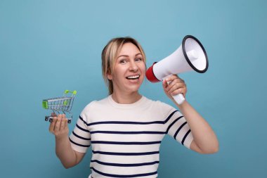 Sarışın, çekici, günlük giysiler içinde genç bir kadın. Mavi arka planda süpermarket tramvayı tutan megafon kullanarak indirimler yapıyor..