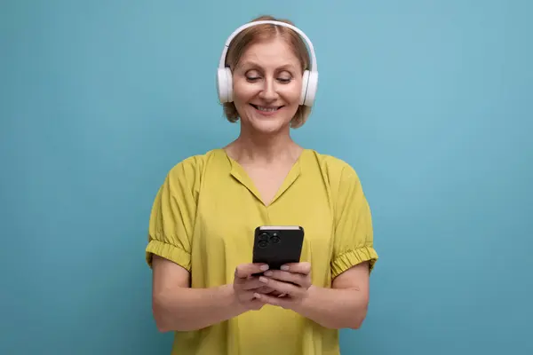 stock image portrait of a blond adult woman with headphones and a smartphone in her hands.