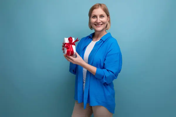 stock image mature woman giving gift for holiday on blue background copy space.