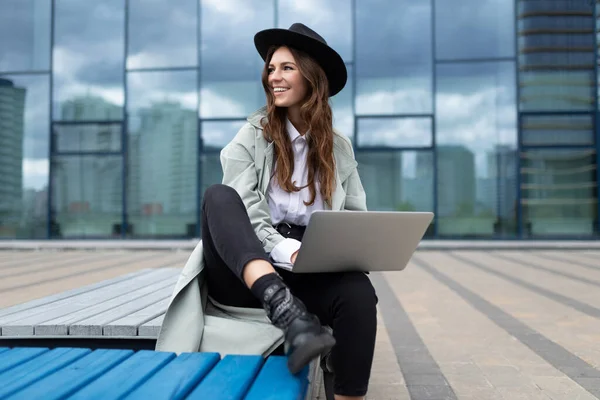 European young woman designer with a laptop in her hands on the background of street buildings.
