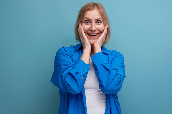 приятно удивлена зрелая женщина в повседневной рубашке на синем фоне.