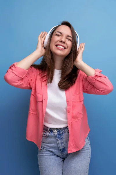 stock image enjoying brunette young woman with dark hair below her shoulders in a shirt and jeans with wireless headphones.