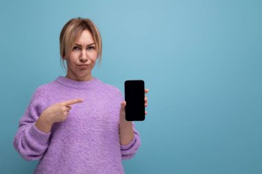 Mor kapüşonlu ciddi sarışın bayan danışman elinde mavi arka planda fotokopi alanı olan akıllı telefon tutuyor..