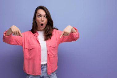 Şok olmuş siyah saçlı kadın stüdyo arka planındaki duvara işaret ediyor..