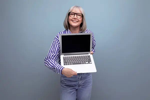 mature woman with gray hair masters remote professions online using a laptop on a bright studio background.