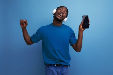 Tişörtlü Afrikalı adam kulaklık ve akıllı telefon kullanarak müzik dinliyor..