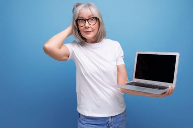 Orta yaş işi. Orta yaşlı, gri saçlı bir kadın uzaktan kumandalı mesleği stüdyo arka planında fotokopi alanı olan dizüstü bilgisayarla yeniden öğreniyor..