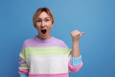 Mavi arka planda pastel renkli çizgili süveter giyen, şaşırmış sarışın genç bir kadının portresi..