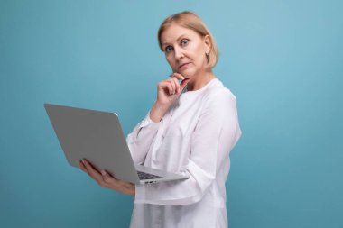 Ciddi, olgun, sarı saçlı bir iş kadını internette dizüstü bilgisayar kullanıyor..