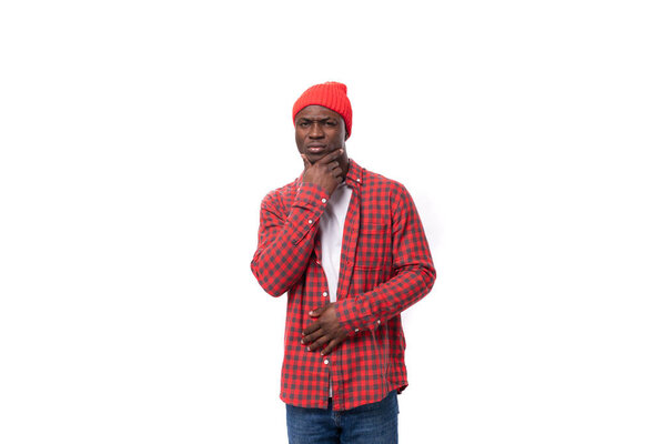 Successful pensive 30s black american man dressed in red shirt and cap on white studio background with copy space.