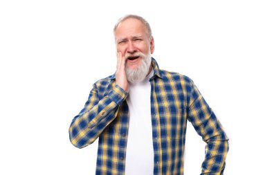 60 'lı yaşlarda, beyaz arka planda sakallı, beyaz saçlı bir adam var..