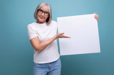 Stüdyo arka planında mokasen olan boş ilan panosu tutan gri saçlı olgun bir kadın..