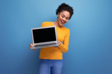 Saçları afro saçlı genç Latin bir kadın stüdyo arka planında dizüstü bilgisayar kullanıyor..