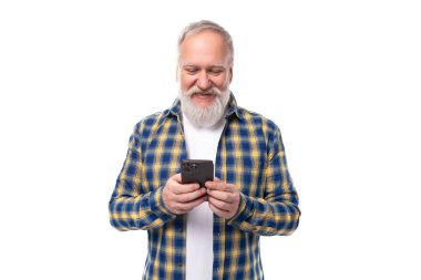 Üst düzey emekli, gri saçlı, sakallı, gömlek ustası, beyaz arka planda akıllı bir telefon..