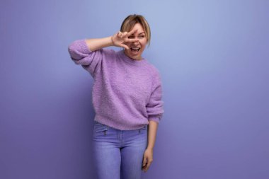 Lavantalı süveter giyen, parlak ve parlak bir arka planda kameraya gülümseyen, enerjik, sarışın genç bir kadının portresi..