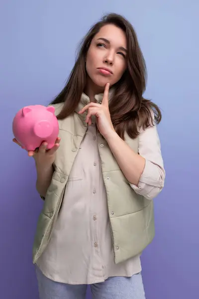 young brunette woman decides where to invest her savings from the piggy bank.