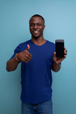Mavi tişörtlü yakışıklı genç Amerikalı adam elinde telefon ve ekran modeli var..