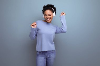 20 'li yaşlardaki enerjik afro esmer kadın stüdyo arka planında beyaz kablosuz kulaklık ve fotokopi alanı kullanarak müzik dinliyor..