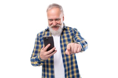 Yakışıklı, beyaz saçlı, sakallı, gömlek üstadları olan bir adam. Beyaz arka planda, fotokopi alanı olan bir akıllı telefon..