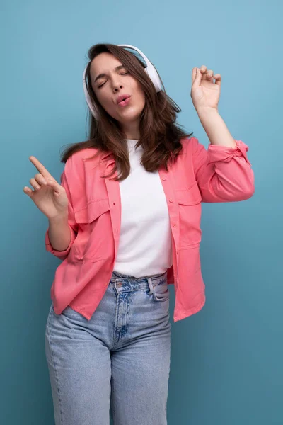 stock image energetic brunette young woman in a shirt and jeans dances to the music from wireless headphones.