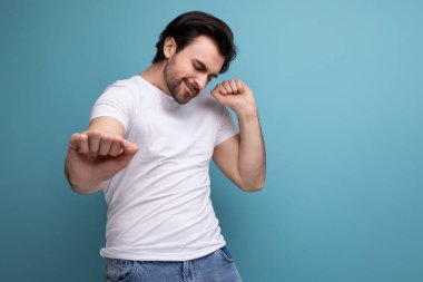 Beyaz tişörtlü esmer bir adam stüdyo arka planında dans ediyor..