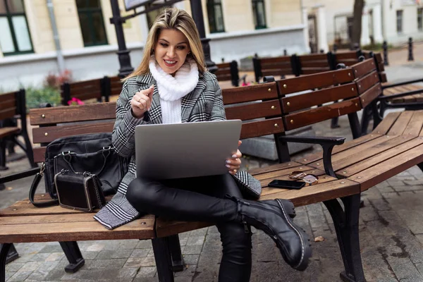 young blond woman journalist with a laptop sits on the terrace in a cafe.