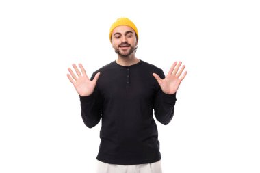 Sakallı, siyah ceketli ve sarı şapkalı çekici, genç bir adam avuçlarını öne doğru gösteriyor..