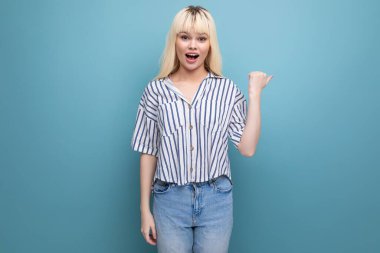 25 yaşında, çizgili bluz ve kot pantolonlu, gülümseyen sarışın bir kadın parmağını yana gösteriyor..