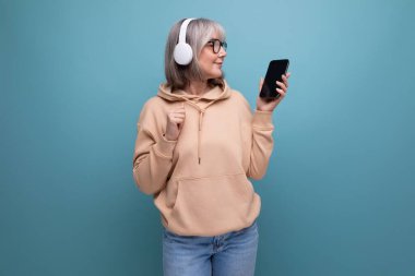 Elinde akıllı telefon olan 60 'lı yaşlarda olgun bir kadın dijital teknolojileri fotokopi çekilen bir stüdyo arka planında okuyor..