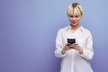 Beyaz bluz giymiş kısa sarı saçlı beyaz ofis çalışanı genç ve güzel bir bayan arka planda fotokopi alanı olan bir akıllı telefon kullanıyor. iş kavramı.