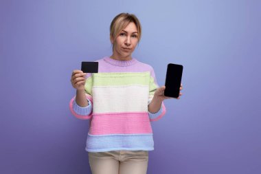 Sarı elbiseli genç bir kadın kredi kartı ve akıllı telefonu gösteriyor. Mor arka planda fotokopi alanı olan bir model..