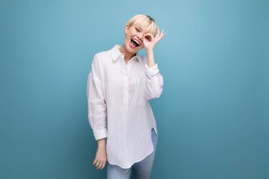 Sarışın, güzel bir ofis çalışanı. Kısa saçlı, beyaz gömlekli, mavi arka planda..