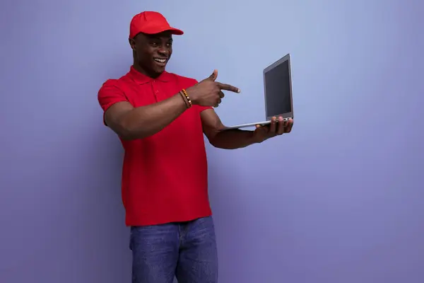 branded clothing concept. american man in red t-shirt and cap holding laptop.
