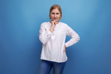 Beyaz gömlekli yetişkin bir kadın stüdyo arka planında gülümsüyor..