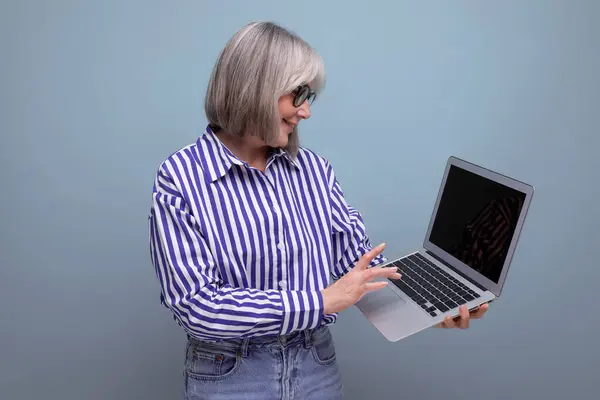60s middle aged woman master remote professions online using laptop on bright studio background.