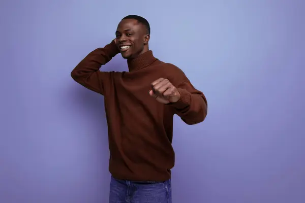 dark-skinned 25 year old guy with a short haircut in a brown sweater laughs on a studio background with copy space.