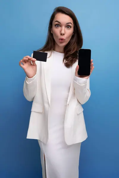 financial worker brunette young woman in a dress and jacket with a payment card for shopping and a smartphone.