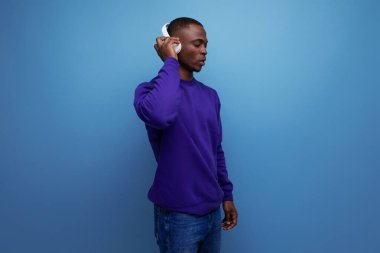 30 'lu yaşlarda mavi kazak giyen koyu tenli bir Amerikalı kulaklıkla müzik dinliyor..