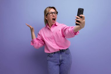 Güzel, sarışın, Avrupalı, at kuyruklu, şık saçlı, pembe tişörtlü ve kot pantolonlu bir kadın model video ekranında konuşuyor..