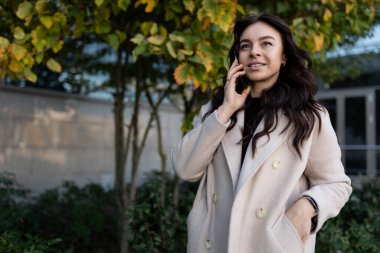 Genç esmer kadın sokakta akıllı telefondan konuşan serbest çalışan..