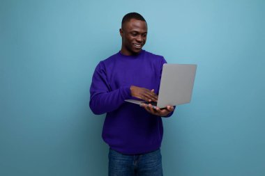 Mavi tişörtlü yakışıklı Afrikalı adam uzaktan bilgisayarla çalışıyor..