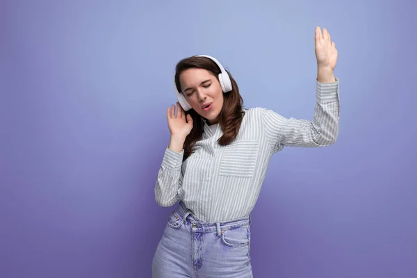 dancing 25 year old brunette woman in a shirt and jeans enjoys music in headphones.
