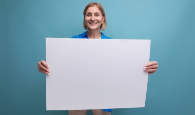 Sarışın, orta yaşlı kadın elinde not panosuyla mavi arkaplan kopyalama alanı oluşturmuş..