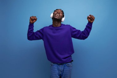 Mavi kazaklı Amerikalı genç adam kulaklıkla müzik dinliyor..